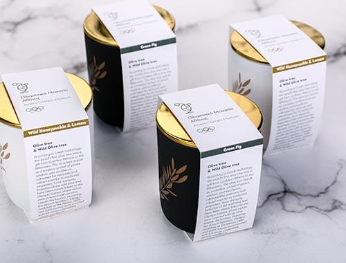 Τέσσερα premium private label κεριά σε λευκό και matte μαύρο γυαλί με χρυσό καπάκι, δημιουργημένα αποκλειστικά για το Ολυμπιακό Μουσείο Αθήνας.